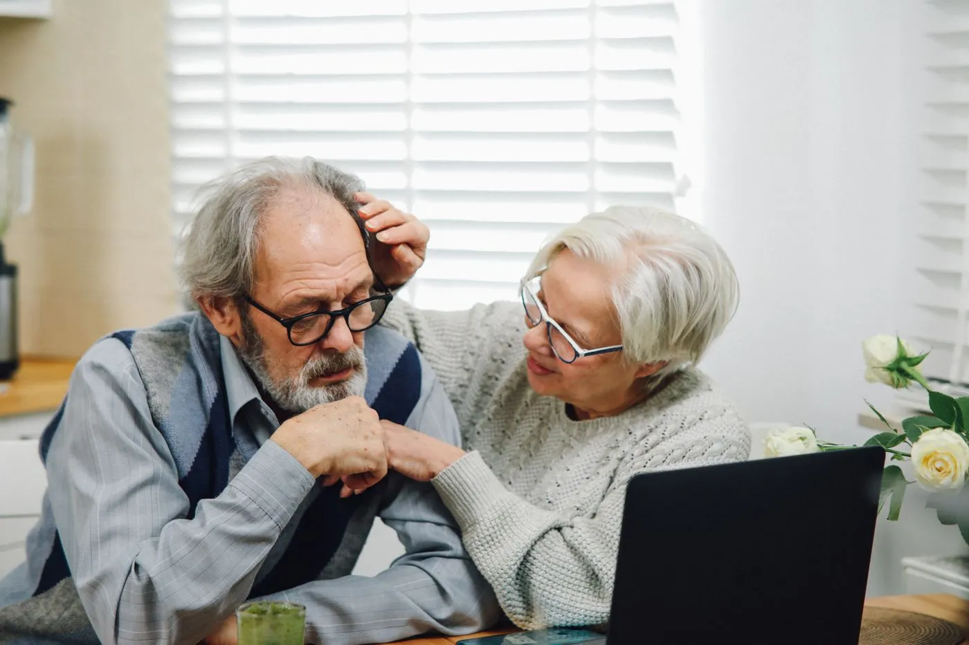 An older couple at a kitchen table looking at a laptop together