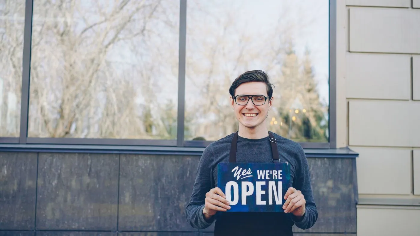 A small-business owner holding a sign that says we're open